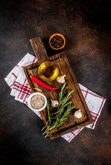 Cooking background, herbs, salt, spices, olive oil on cutting board, dark rusty background copy space top view