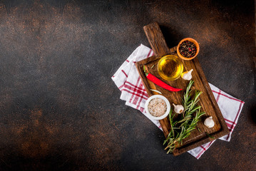 Cooking background, herbs, salt, spices, olive oil on cutting board, dark rusty background copy space top view