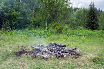 Burned bonfire on a green glade, among the forest.