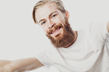 Close up portrait of a cheerful bearded man taking selfie over white background