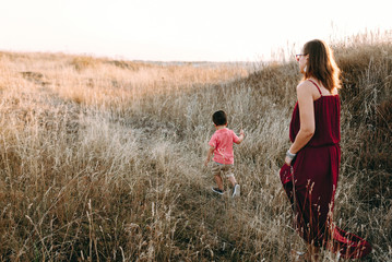 beautiful young mother in a long red dress easy walks with her young son. Summer, sunset, high yellow grass, mountain locality, tenderness