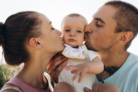 Wide portrait of happy family. Father and mother kiss her liitle baby son on the cheeks