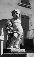 Statue of Bacchus (Dionysus) with grapes in his hands against rough stone wall. Garden sculpture. (Provence, France). Black and white photo.