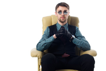 portrait of stylish spy in sunglasses and gloves sitting in armchair isolated on white