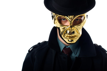 portrait of criminal in golden mask, hat and black coat looking at camera isolated on white
