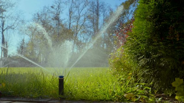 Close-up of a nozzle for spraying water by automatic watering system for lawn with lush green grass in sunny day. Slow motion. HD