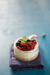 Cheesecake with a top filled  of berries  on a jar over a black background rusty, natural light only.