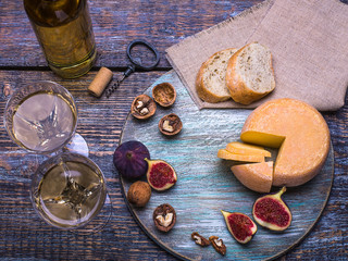 White wine in a bottle, wine glass, cork, bottle screw and a set of products - cheese, grapes, nuts, olives, figs on a wooden board, background