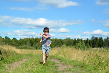 The boy is running barefoot along the trail in the field.