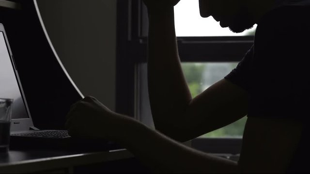Sad man silhouette typing on laptop, unemployment problem, break up depression