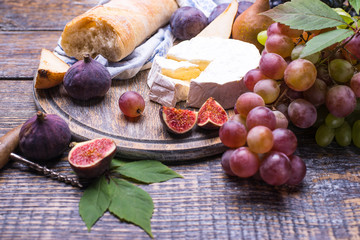Wine in a bottle, cork, bottle screw and a set of products - cheese, grapes, nuts, olives, figs on a wooden board, background