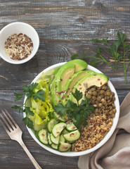Green Buddha Bowl with lentils, quinoa, avocado, cucumber, fresh lettuce, herbs and seeds. Delicious healthy balanced eating. On a wooden background, top view