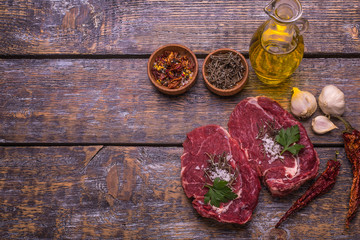 Raw beef meat, grilled beefsteak, salt, hot pepper, garlic, tomato, thyme, rosemary on a wooden board, background.