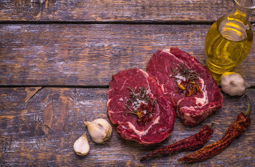 Raw beef meat, grilled beefsteak, salt, hot pepper, garlic, tomato, thyme, rosemary on a wooden board, background.
