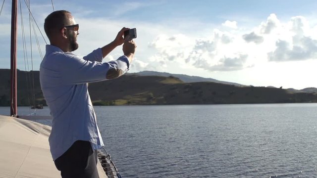 Young man taking photos with cellphone sailing yacht, super slow motion
