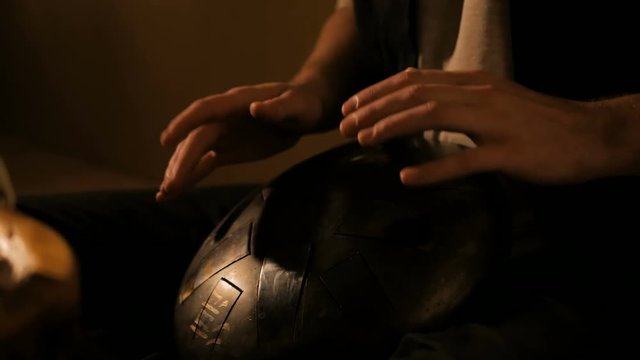 Man playing tank drum or hang at home. Warm romantic illumination, low key. Relaxation, meditative and traditional music concept. Close up shot