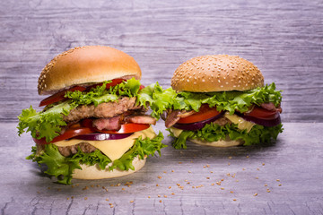Craft beef burger and fresh vegetables, tomatoes, onion, salad, cheese,  on wooden table isolated on gray background.