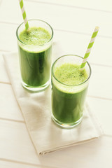 Healthy green smoothie made from spinach, apple and cucumber in a jars with red straw on white wooden table. Toned