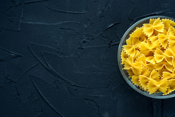 farfalle macaroni Pasta in a glass cup on a black textured background from the side. Close-up with the top. With space for text.