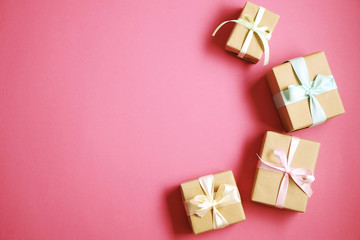 Simple composition with multiple presents wrapped in hand made blank craft paper gift wrap, pastel satin bow. Simple giftbox, wrapping, giftwrap, silk ribbon. Pink background, close up, copy space.