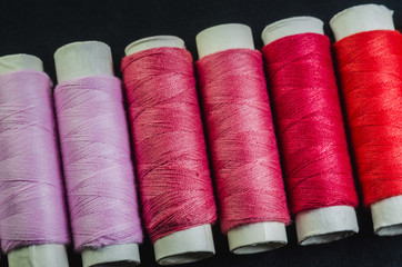 Spools of pink and red threads on black fabric