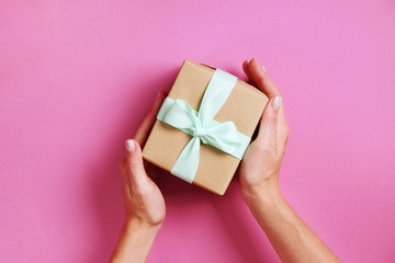 Young woman holding bunch of presents wrapped in hand made blank craft paper gift wrap, satin bow. Female hands, simple giftbox, wrapping, giftwrap, silk ribbon. Pink background, close up, copy space.