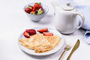 Openwork thin cheese crepes served with strawberry on grey concrete background. Homemade pancakes. Delicious breakfast