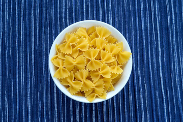farfalle macaroni Pasta in a white cup on a striped white blue cloth background in the center. Close-up with the top.