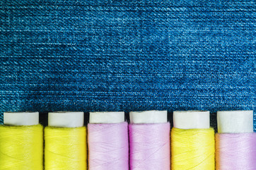 Spools of yellow and pink threads on denim