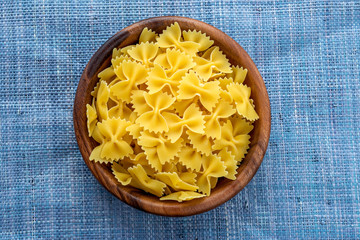 farfalle macaroni pasta in a wooden bowl on a blue knitted background in the center. Close-up with the top.