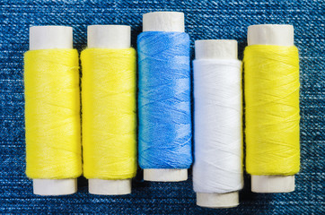 Spools of blue, yellow and white threads on denim