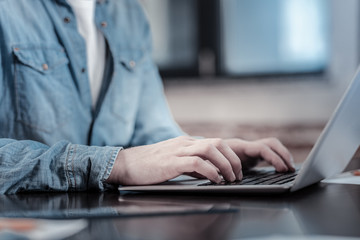 Online communication. Close up of male attractive strong hands placed on keyboard while laptop standing on surface