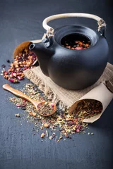 Foto op Aluminium Black ceramic teapot with tea,Different tea and herbs , dried rose flowers on dark concrete background. © OlegKovalevich