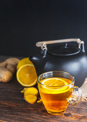Healing Tea with ginger and lemon . Transparent Cup with black teapot on wooden background.