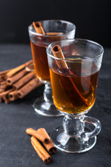 Freshly brewed black tea with cinnamon, in transparent cups on a dark background.