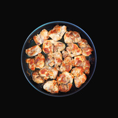 Pieces of roasted meat in a frying pan isolated on black background. Top view