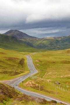 Curved winding road between Scottish Glenshee hills with blue clouds on the horizon in Cairngorms National Park
