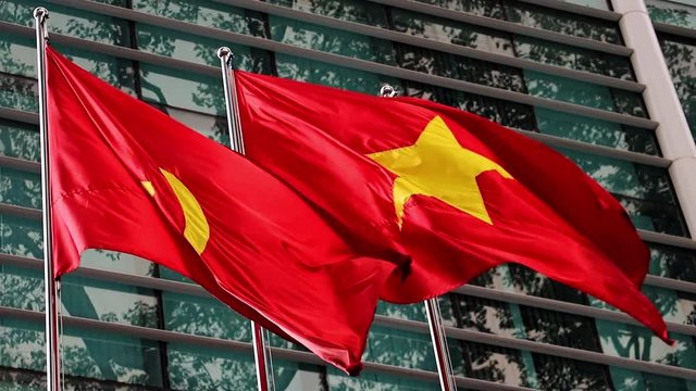 The red flag with communist symbols of a sickle and a hammer flying by building.The Red flag with a five-pointed star flutters on the pole.