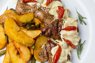 Baked chicken meat. With fried potatoes, pesto sauce and vegetables. In a round plate. View from above. Close-up