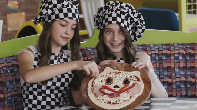 Two young girl with smile presentating a pizza for camera
