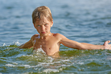 Portrait of young serious boy swimming in the lake at summer © Denys Kurbatov