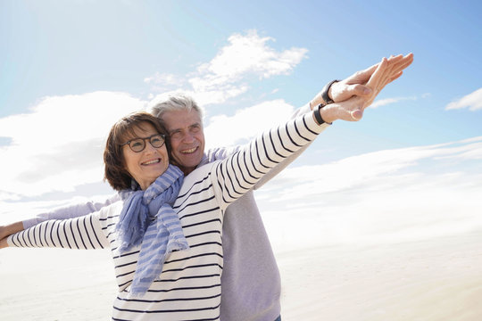 Portrait of senior couple at the beach stretching arms out