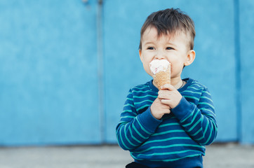 Fototapeta premium baby outdoor on blue wall background eating ice cream