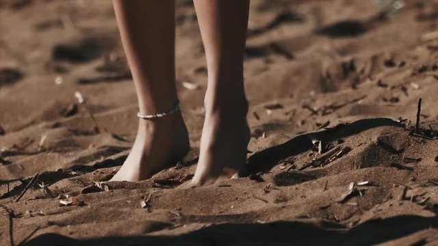 Young sexy girl in pareo bare feet with ankle jewelry stomping on beach sand, sunny summer day outside