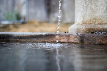 Makroaufnahme von vielen kleinen Wassertropfen, welche in einen alten, leicht schmutzigen Brunnen aus Stein fallen