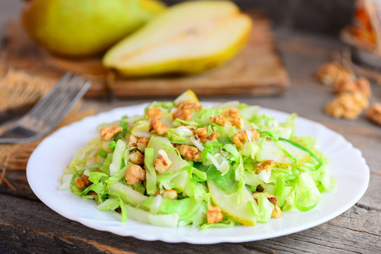 Pear and cabbage slaw. Home salad with fresh pear, cabbage and walnuts on a plate. Rustic wooden background. Easy healthy food. Closeup