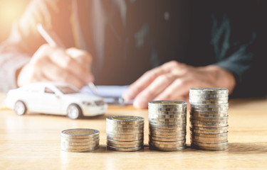 Men are Saint documents about cars  with  some coins calculator and car toy on desk.