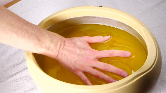 Close up slow motion shot of unrecognizable woman putting hand into paraffin bath taking care of hands skin.