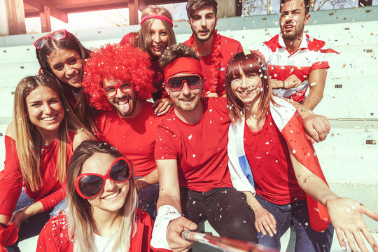 group of fans dressed in red color takes a selfie in the stand