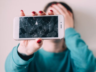 Broken glass screen smartphone in hand of upset girl, white background